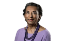 Dr. Anna Eliatamby smiling, wearing a light purple shirt and layered purple necklace, with short hair, on a plain white background.