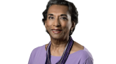 Dr. Anna Eliatamby smiling, wearing a light purple shirt and layered purple necklace, with short hair, on a plain white background.